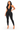 A woman modeling a black halter-neck, one-piece jumpsuit with a deep plunging neckline, photographed against a solid white background.