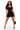 A woman modeling a black halter-neck bodycon mini dress against a plain white studio background, holding a small black handbag and wearing clear high-heeled sandals.