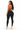 A woman modeling a black one-piece jumpsuit from the back, featuring a lace-up back design, on a solid white background.