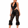 A woman modeling a black lace two-piece outfit consisting of a halter crop top and matching high-waisted flared cropped pants with ruffled hems, paired with black high-heeled sandals against a plain white background.