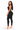A woman modeling a black sleeveless bodycon jumpsuit with a high-cut leg and side cutout details, paired with clear high-heeled sandals, against a plain white background.